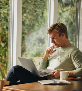 Jak si půjčit a nedostat se do potíží - muž sedí u okna s počítačem a přemýšlí