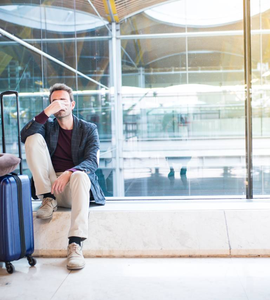 Ospalý muž s kufrem na letišti - jet lag