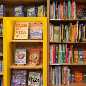 Bookshelves filled with colorful children's books, educational books, and activity kits, with a yellow display section in the center.