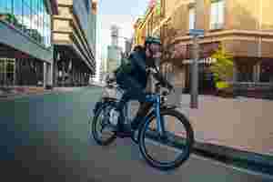 Mand med hjelm på elcykel kører ind i et sving i byen