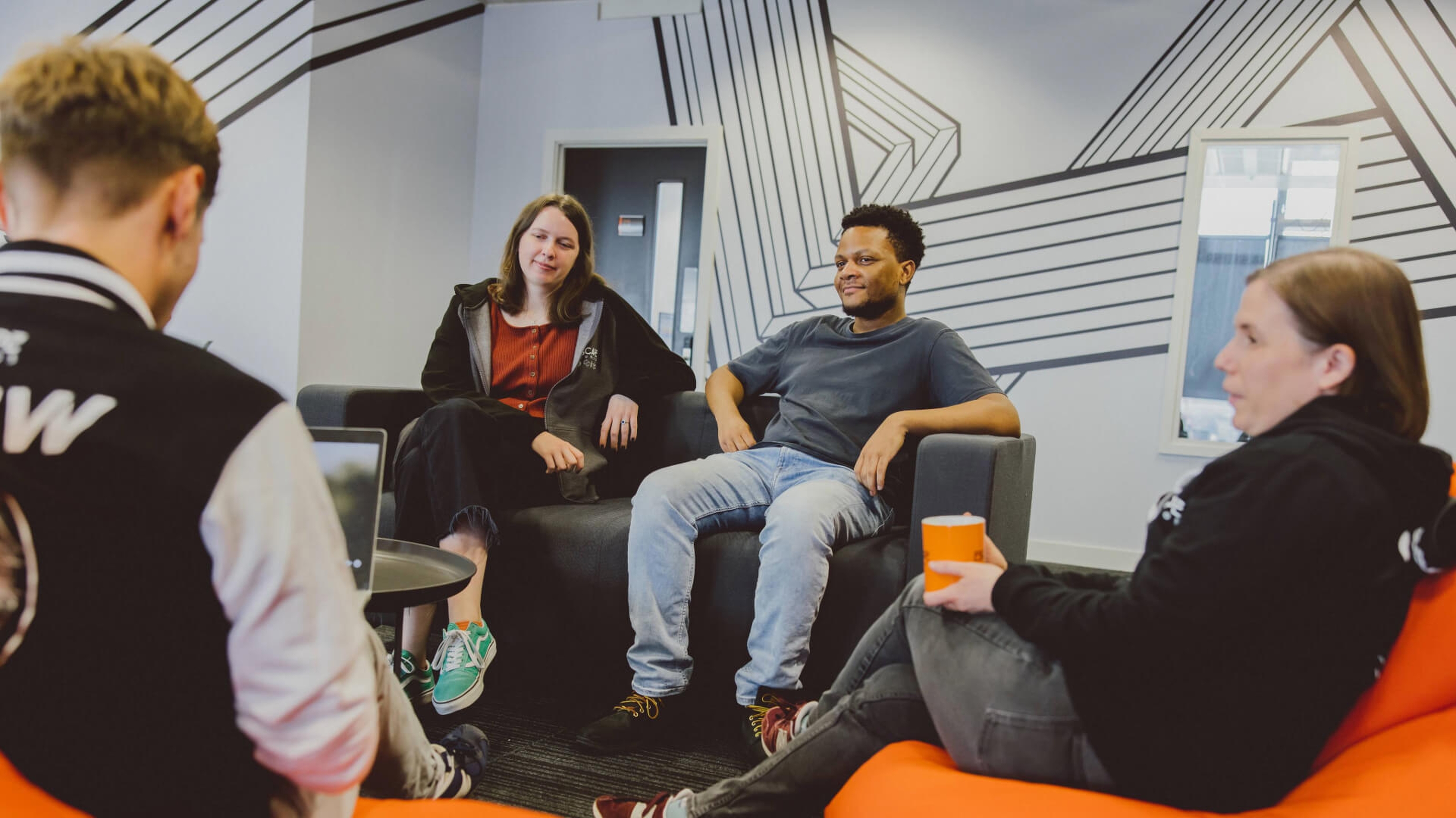 A group of four postgraduate students relaxing on orange beanbags and a grey sofa