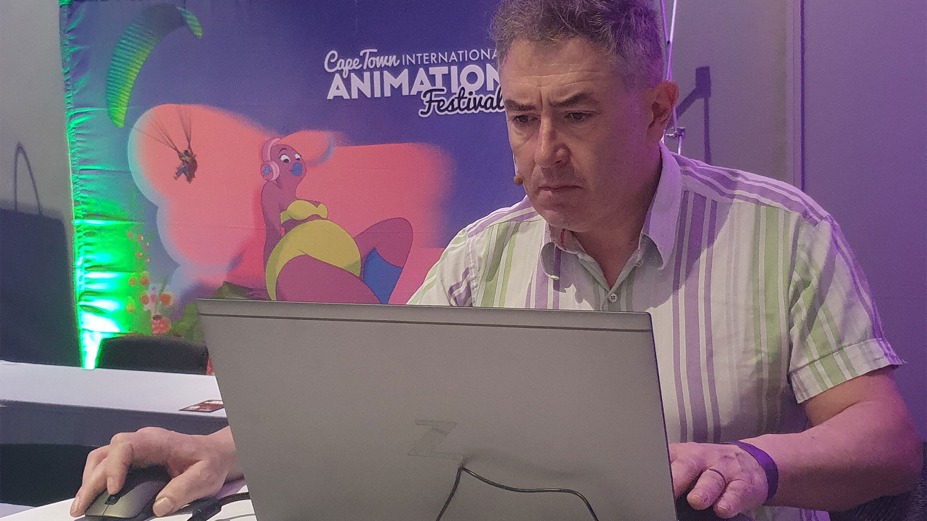 Houdini Tutor Simon Browne sat at a laptop with a Cape Town International Animation Festival banner in the background