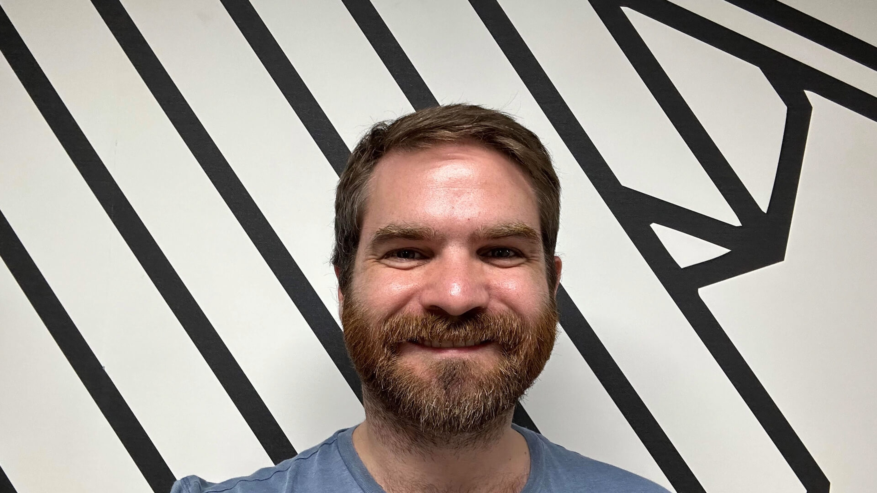 Gregor, smiling in front of a black and white stripy Escape Studios wall
