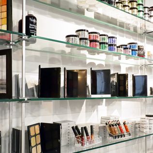 Various makeup products are lined up neatly along glass shelves held up by metal cables and rods.