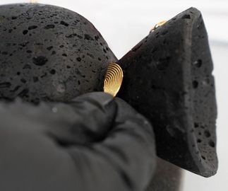 gloved hand placing a gold, arch-shaped detail onto a black basalt sculpture