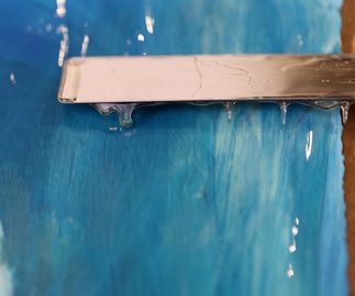 metal spatula spreading viscous resin over the surface of a vibrant blue print