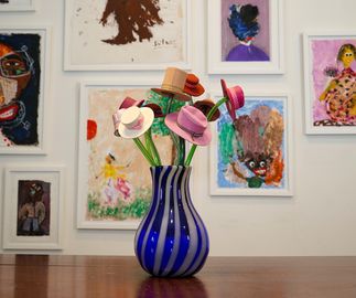 glass vase with hats on a table in front of an array of paintings