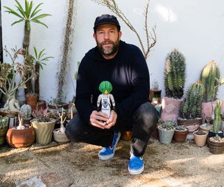 Darren Romanelli crouching holding Cactus Man figurine