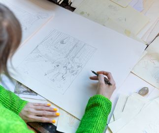Jessie Makinson draws in pencil sitting at her desk in her studio