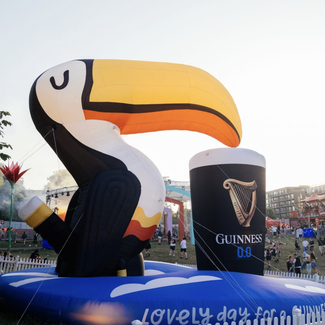 Inflatable toucan and a large Guinness beer can in a festival setting with people and tents in the background.