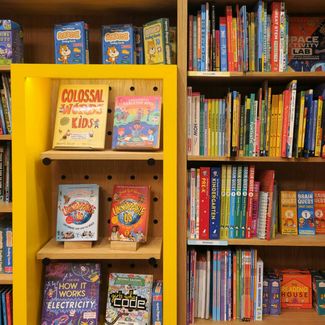 Bookshelves filled with colorful children's books, educational books, and activity kits, with a yellow display section in the center.