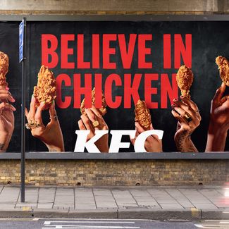 sign reading 'believe in chicken. kfc' with people holding up chicken drumsticks
