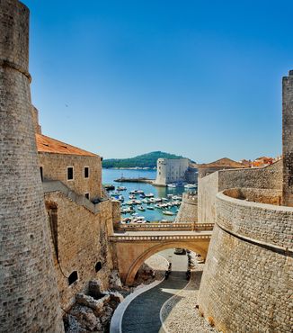 tan stone walls in dubrovnik leading down to a marina filled with sail boats