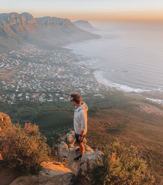 traveler standing on cliff overlooking coast of cape town at sunset