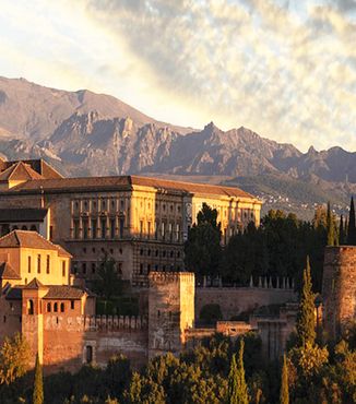 sun shining on stone buildings in granada spain surrounded by mountains