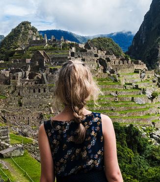 woman with braided hair looking out at people walking around macchu picchu in perun