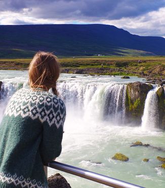 woman looking out at godafoss waterfall in iceland on a sunny day