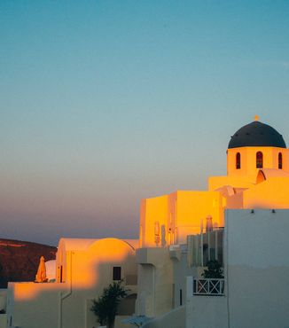 white domed building in greece with sun shining on it