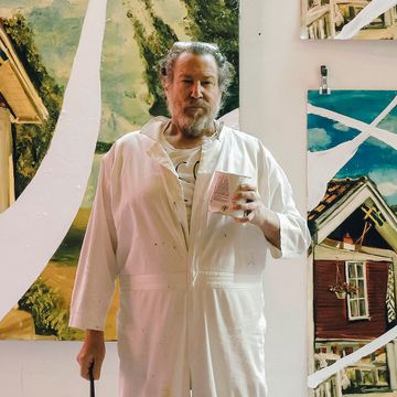 julian schnabel wearing white overalls, holding a can of white paint and a brush