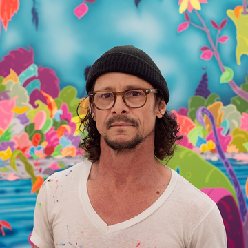 Erik Parker stands infront of his painting wearing glasses, beanie and white tshirt 