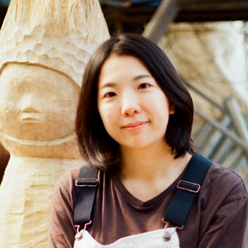 Moe Nakamura portrait infront of wooden sculpture