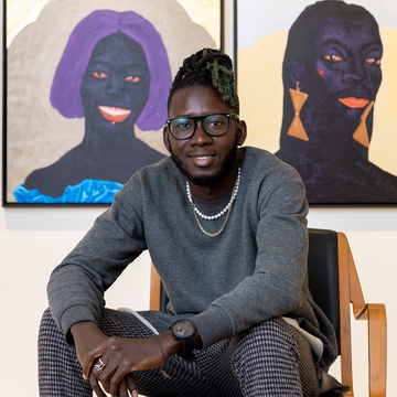 Kwesi Botchway sitting and smiling with his portraits behind him