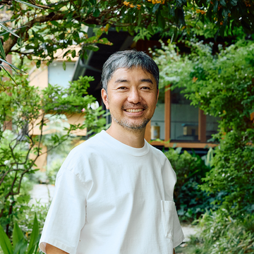 Yu Nagaba standing in a garden outside his studio smiling 