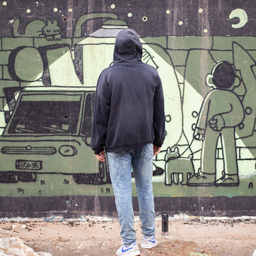 Imon Boy standing in a hoodie facing a graffiti wall