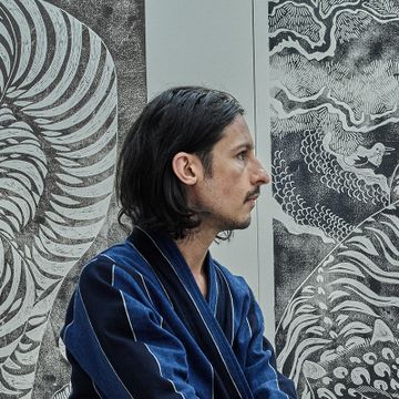 Side-profile of Kour Pour with his art behind him