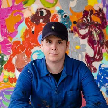 Szabolcs Bozó sitting in blue overalls wearing a cap in his studio