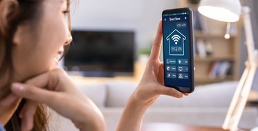Internet věcí - Žena drží mobil a ovládá chytrou domácnost