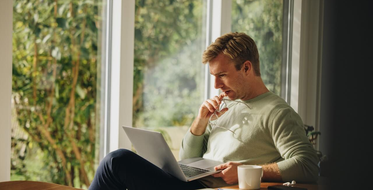 Jak si půjčit a nedostat se do potíží - muž sedí u okna s počítačem a přemýšlí