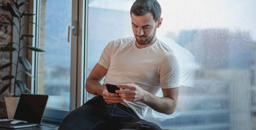 Spotřeba mobilních dat - Muž sedící na okně s mobilem v ruce