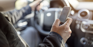 muž sediaci za volantom auta drží mobil v ruke