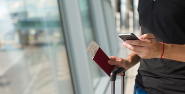 Muž s letenkami, pasem a mobilním telefonem na letišti