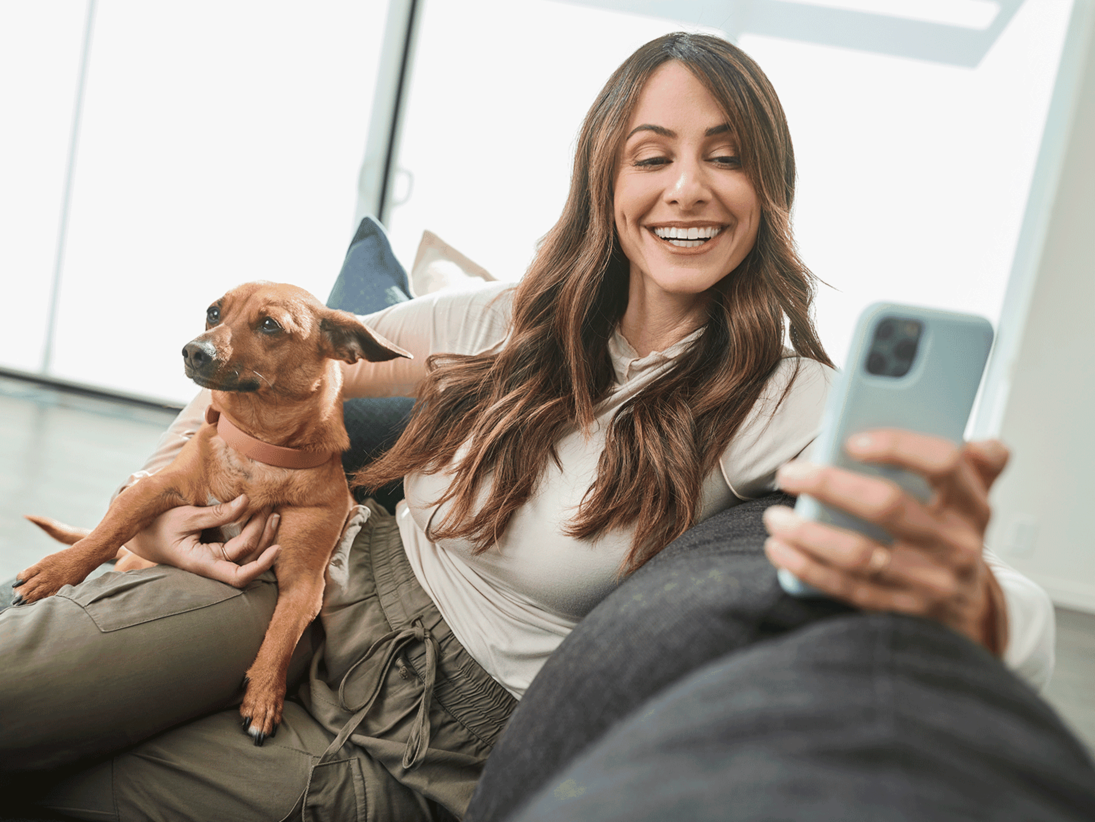Owner looking at her phone screen with her dog beside her, on the sofa.
