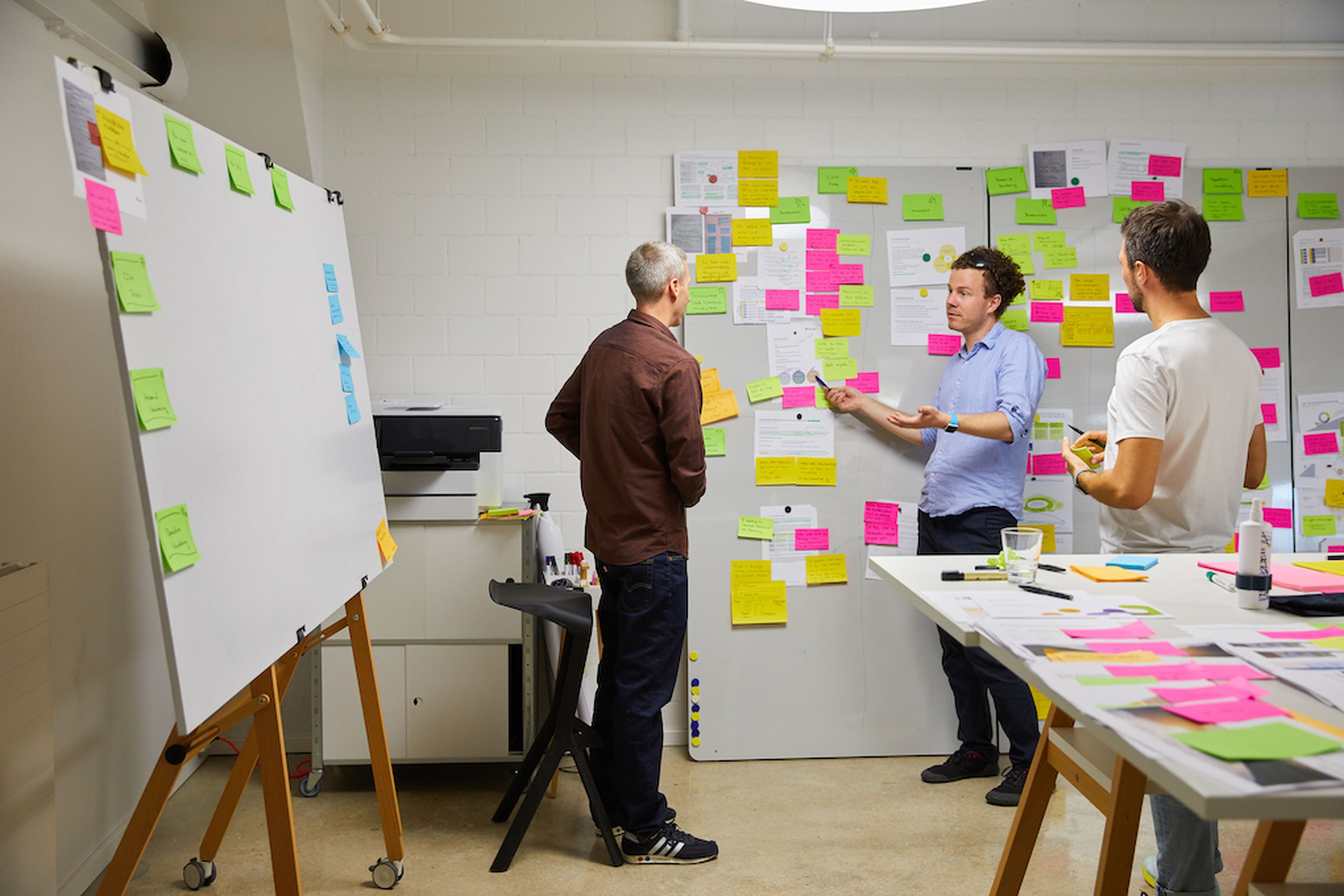 Three people have an inspiring discussion in a room surrounded by post-it notes