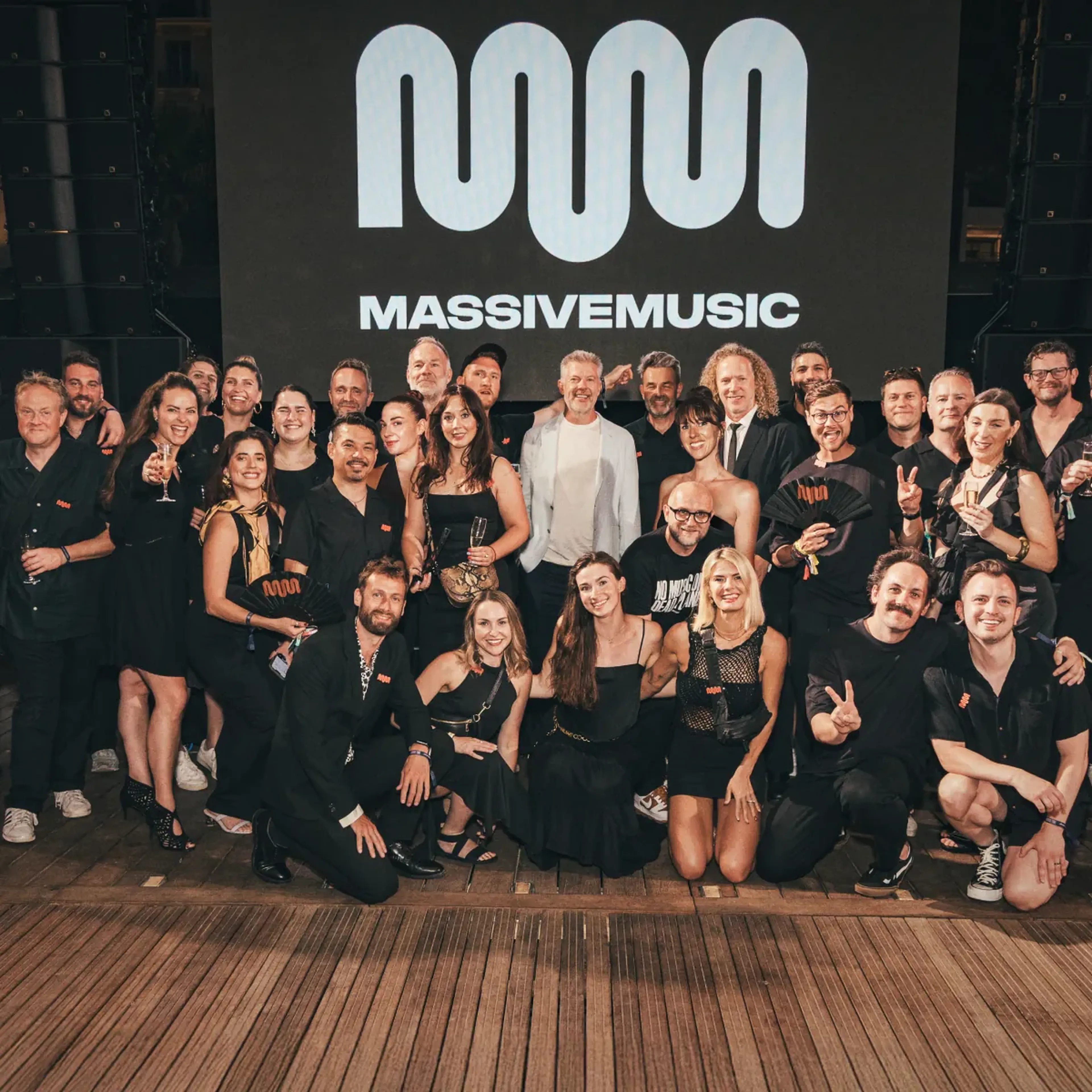The MassiveMusic team together at a summer party in front of the MassiveMusic logo wall