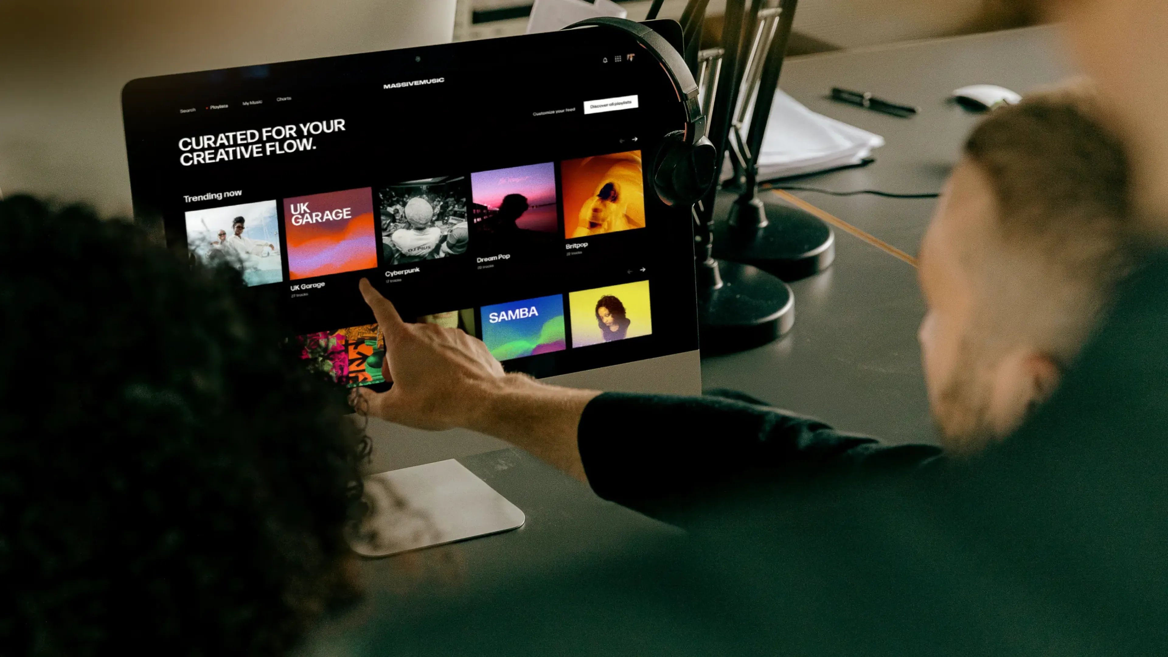 Two people choosing from MassiveMusic playlists on a studio monitor, fully cleared music ready to publish