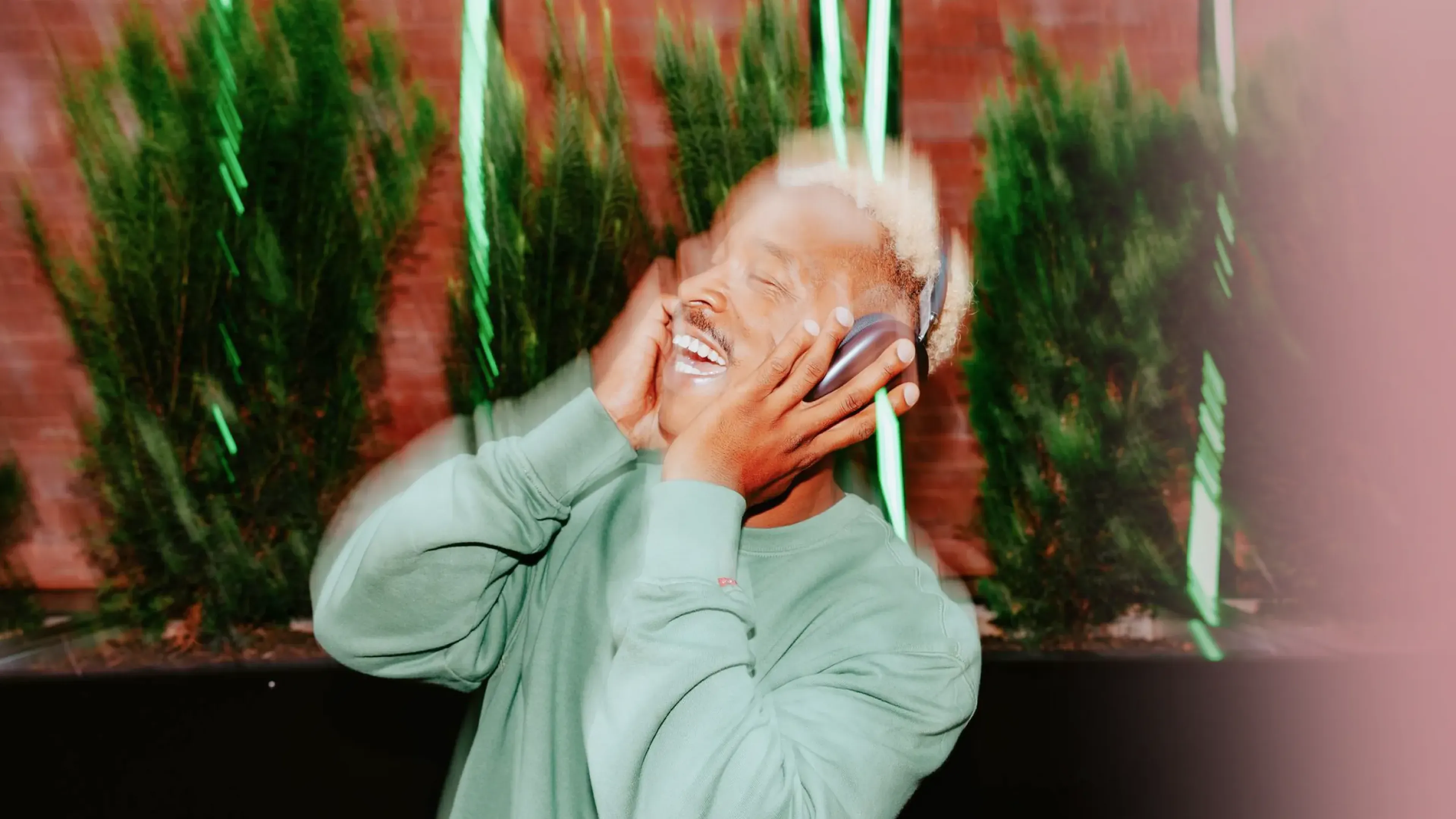 Man laughing as he listens on headphones by a green hedge, a brand sonic identity that makes an impression