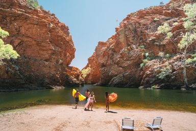 Four people running towards water with inflatable water toys