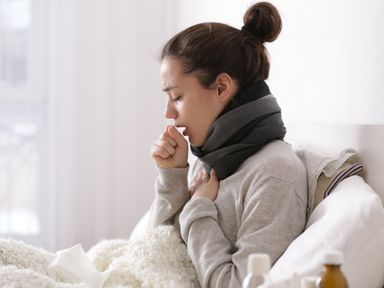Frau mit Schal liegt mit einer Erkältung im Bett und hustet