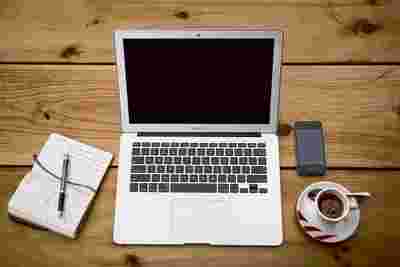 Laptop, Notizbuch, Mobiltelefon und Kaffeetasse auf einem hölzernen Schreibtisch