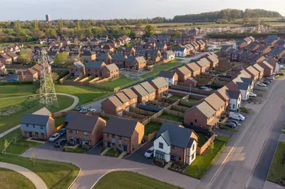 Umlegungsverfahren: Blick auf eine bebaute Fläche mit Einfamilienhäusern und viel Grünfläche. In der Ferne ist eine Kleinstadt zu sehen.