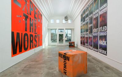 installation view of white gallery space with an orange box in the centre and two large textual artworks on opposing walls