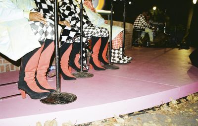 a row of feet wearing red and black suede boots on a round-edged pink stage