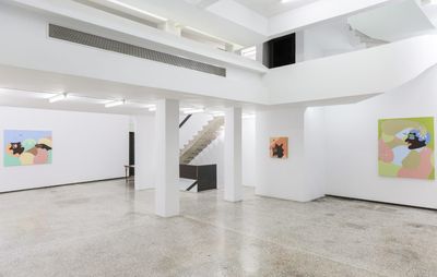 Three colourful paintings hang in a large, open space with white walls and a staircase in the centre against the back wall