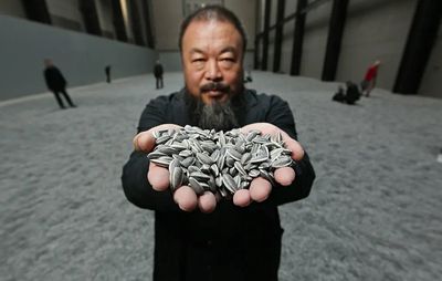Artist Ai Weiwei at the Tate holding up sunflower seeds created from porcelain 