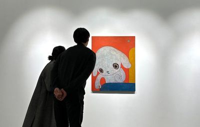 installation view of a painting hung up with two visitors leaning towards it