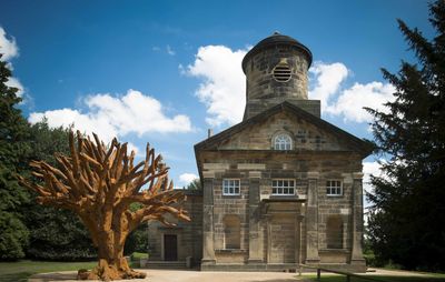 large tree sculpture by Ai Weiwei outside of a small stone chapel